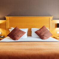 Modern hotel room with plush king bed, stylish wood headboard, striped cushions, warm lighting, cosy atmosphere.