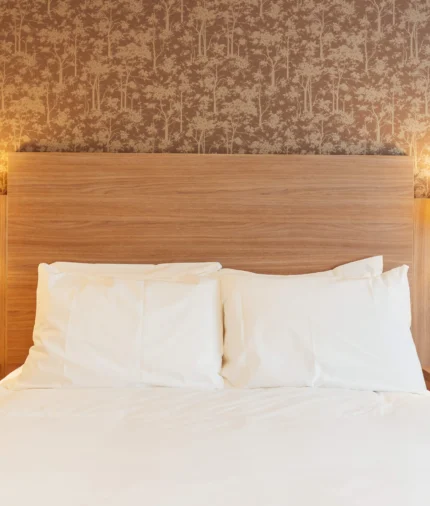 King-size bed with crisp white linen, wooden headboard, bedside lamps, power sockets and phone — cosy boutique hotel room.